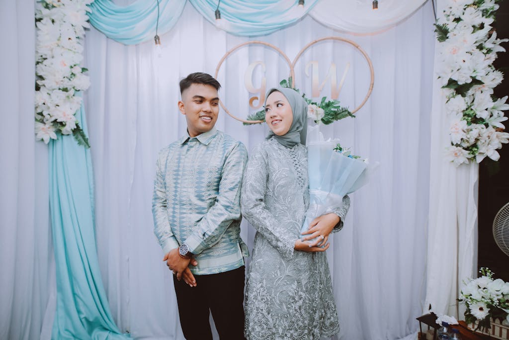 Engaged couple in matching attire smiling joyfully in a floral-decorated setting.